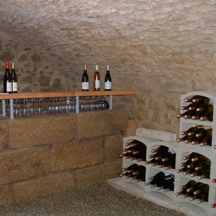 Wine bottles on a wooden shelf and stone wall in a wine cellar.
